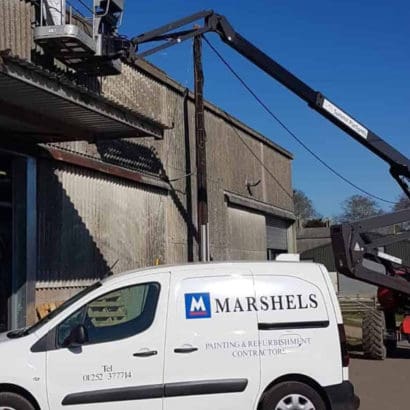 painters using crane to refurbish commercial property exterior alongside their white contractors van