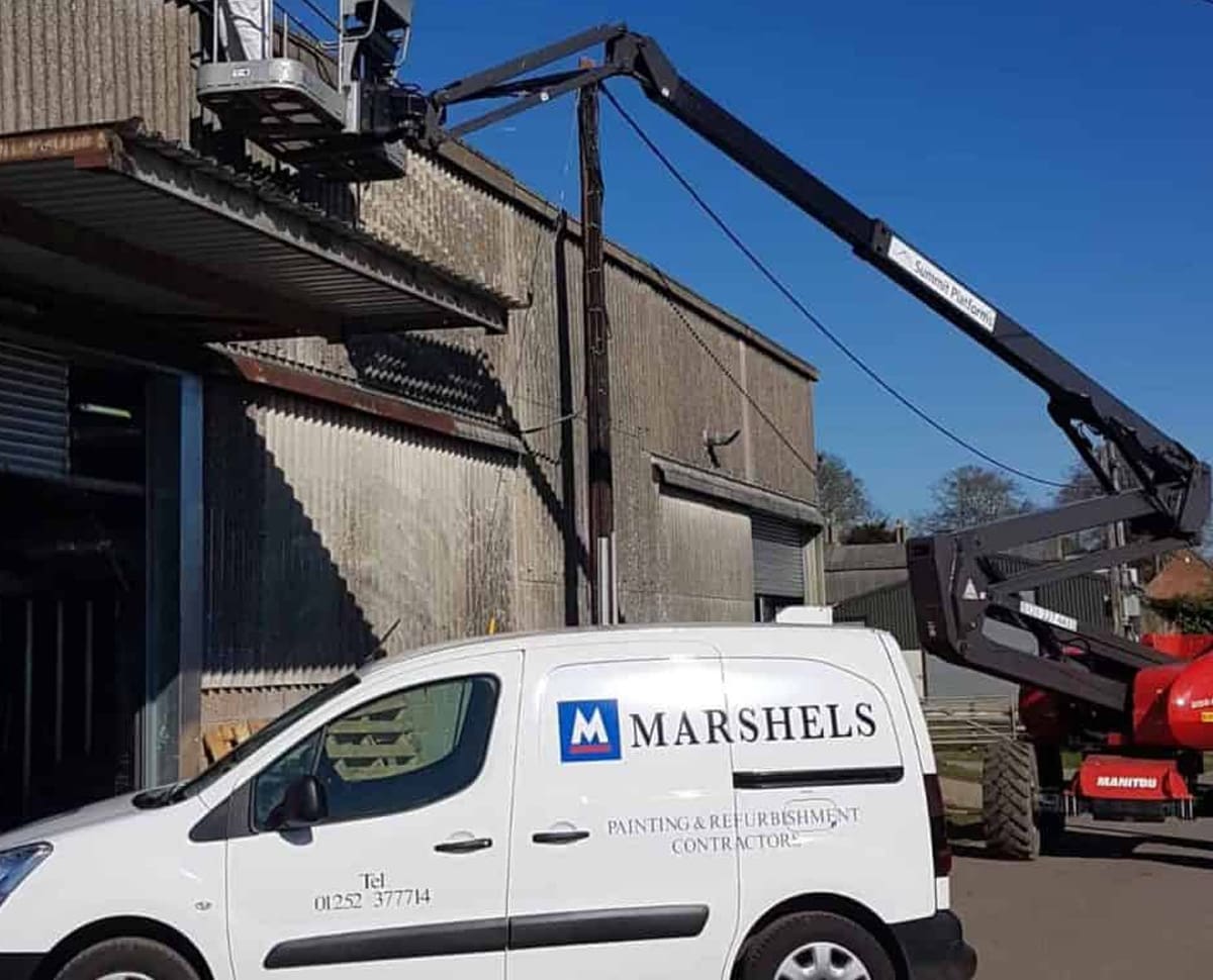 painters using crane to refurbish commercial property exterior alongside their white contractors van