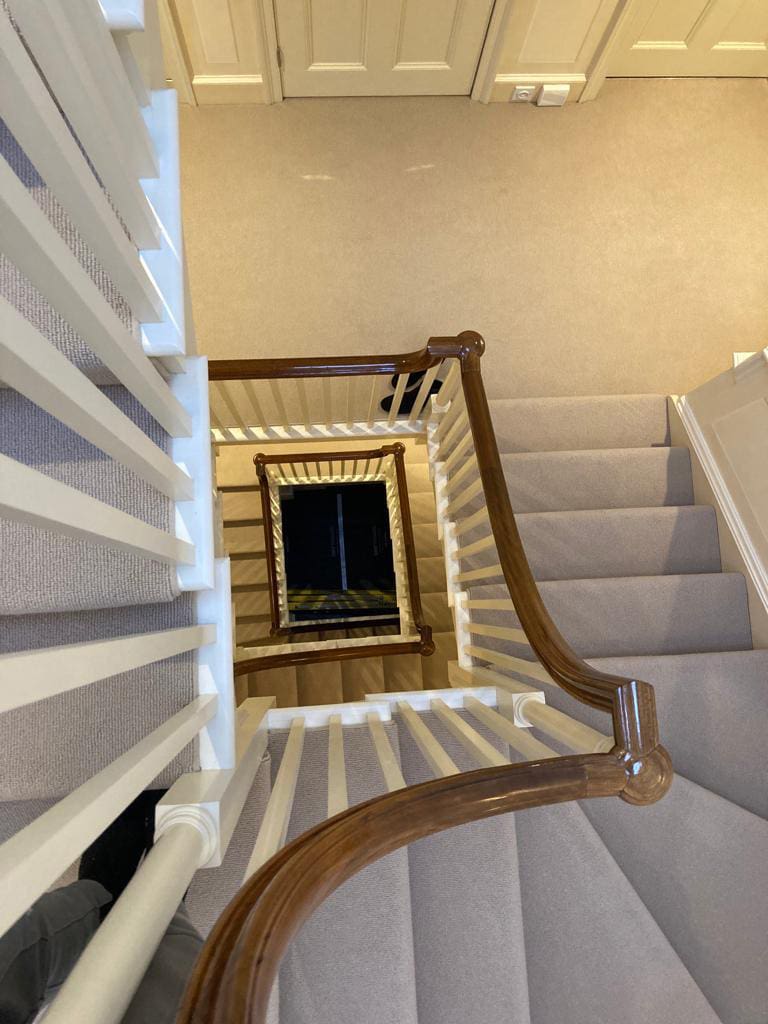 Refurbished staircase by painter and decorator in Surrey featuring a glossy wooden banister and white spindles.